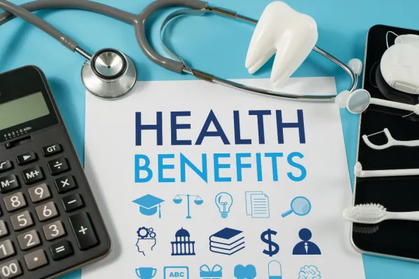 A calculator, stethoscope, and piece of paper that reads "Health Benefits" overlayed on blue background 
